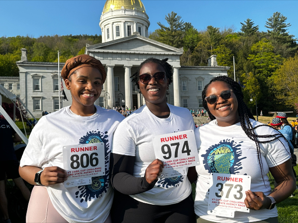 Three people standing in front of the Vermont Statehouse holding numbered race bibs